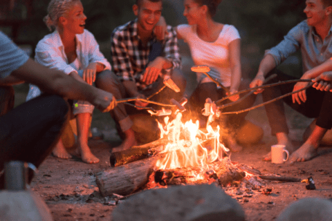 friends laughing while roasting smores over fire at campsite